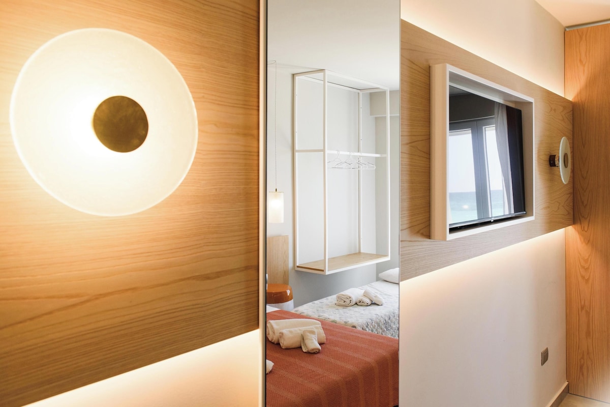 Een moderne hotelkamer met een grote ronde lamp, een kledingkast, een bed met een rode deken en een raam met gordijnen.