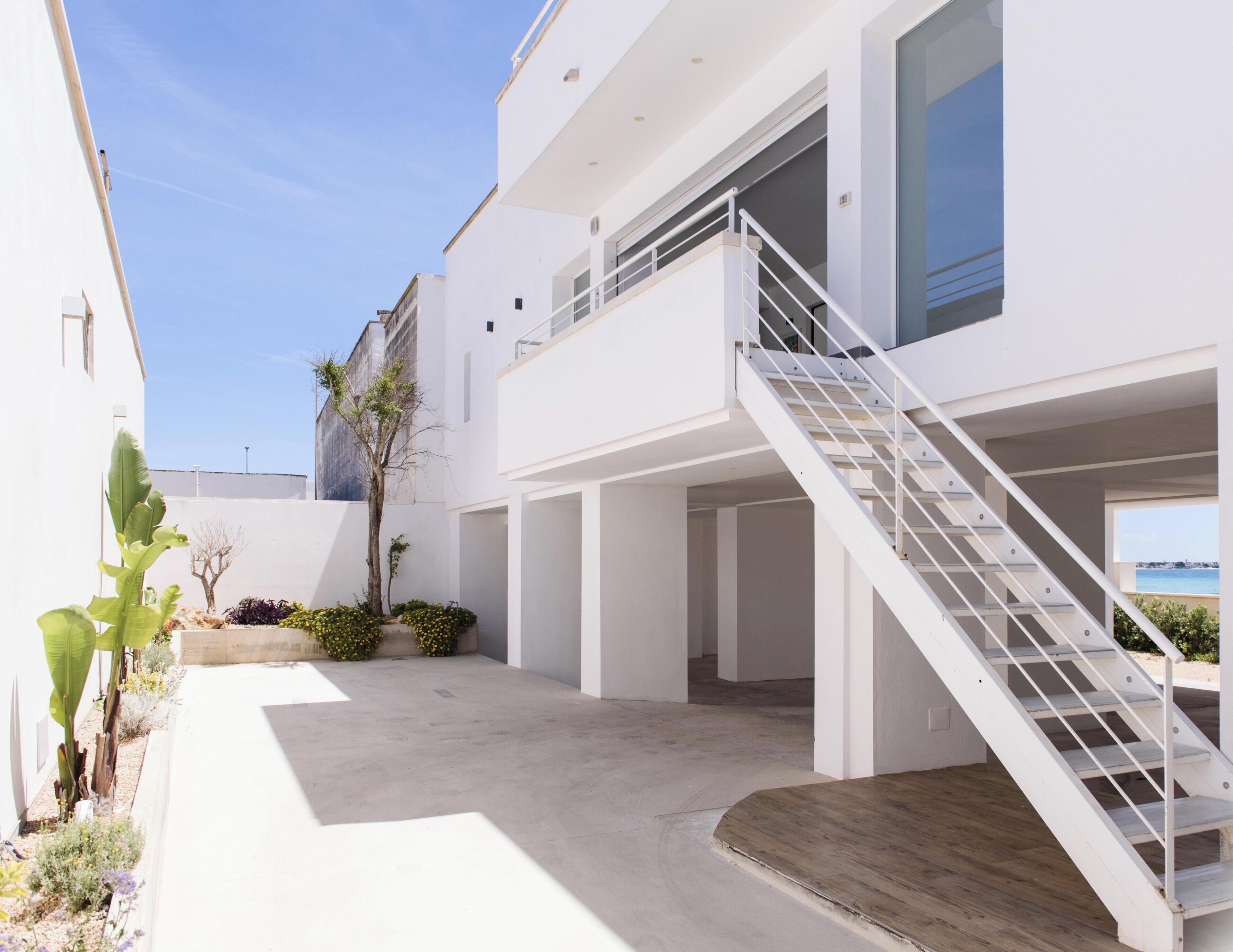 Un bâtiment moderne à l’extérieur blanc, avec un escalier menant à un balcon et une vue sur la mer.