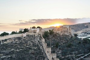 Un castillo histórico con muralla y torres fortificadas, ubicado en una colina con poca vegetación.