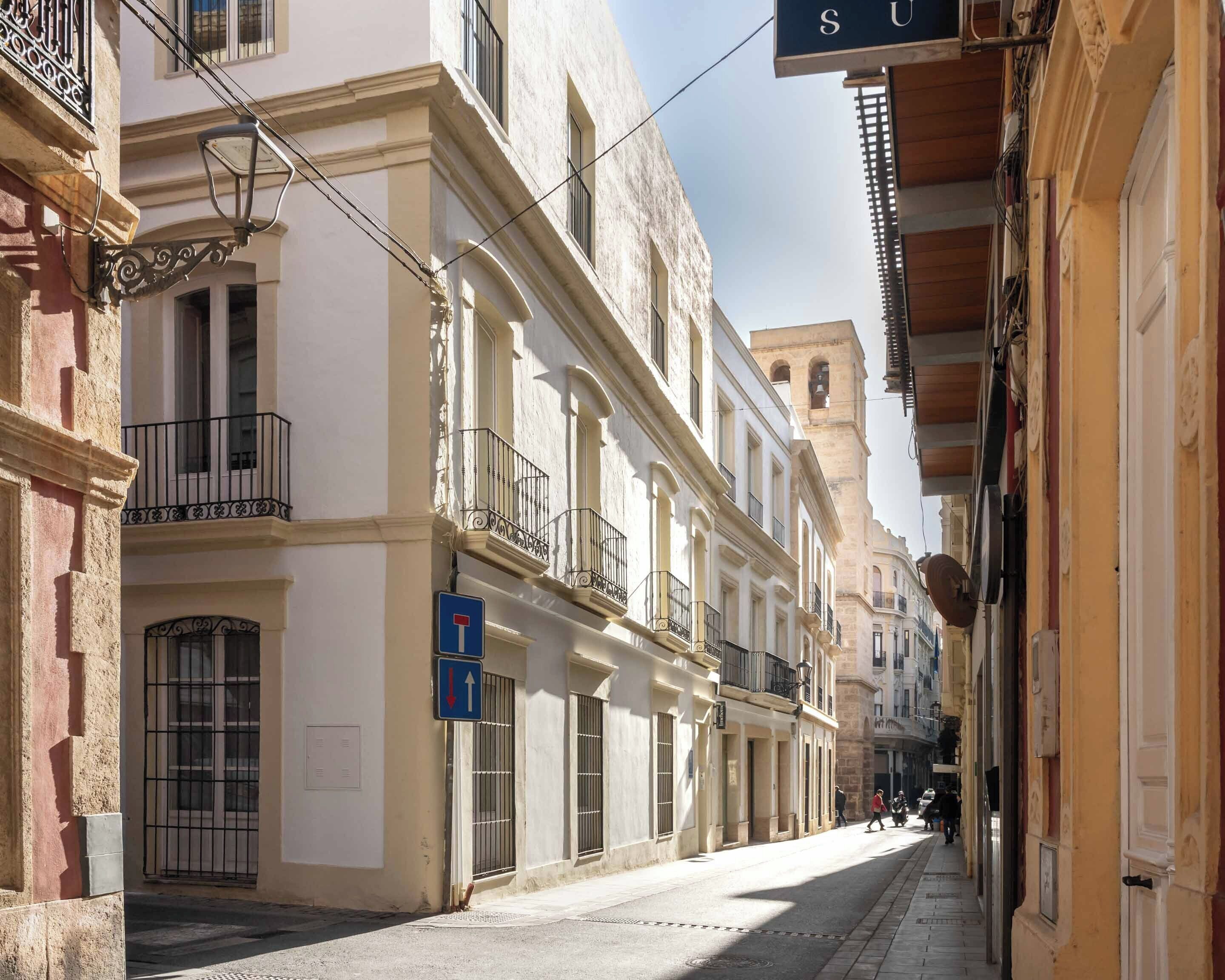A narrow street lined with historic buildings, featuring balconies and a clear sky.