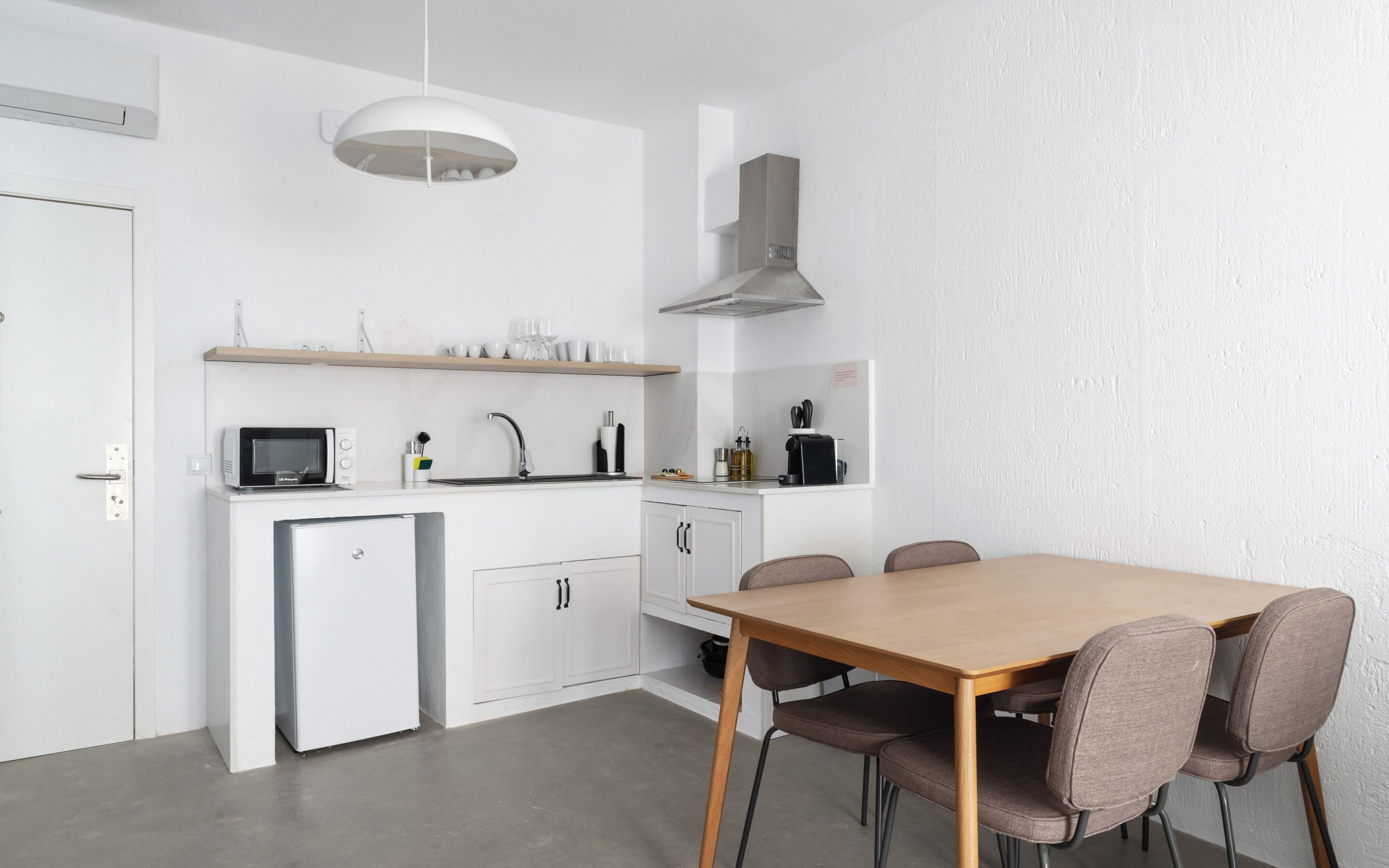 Una cocina moderna con armarios blancos, un microondas integrado y una mesa de madera con cuatro sillas.