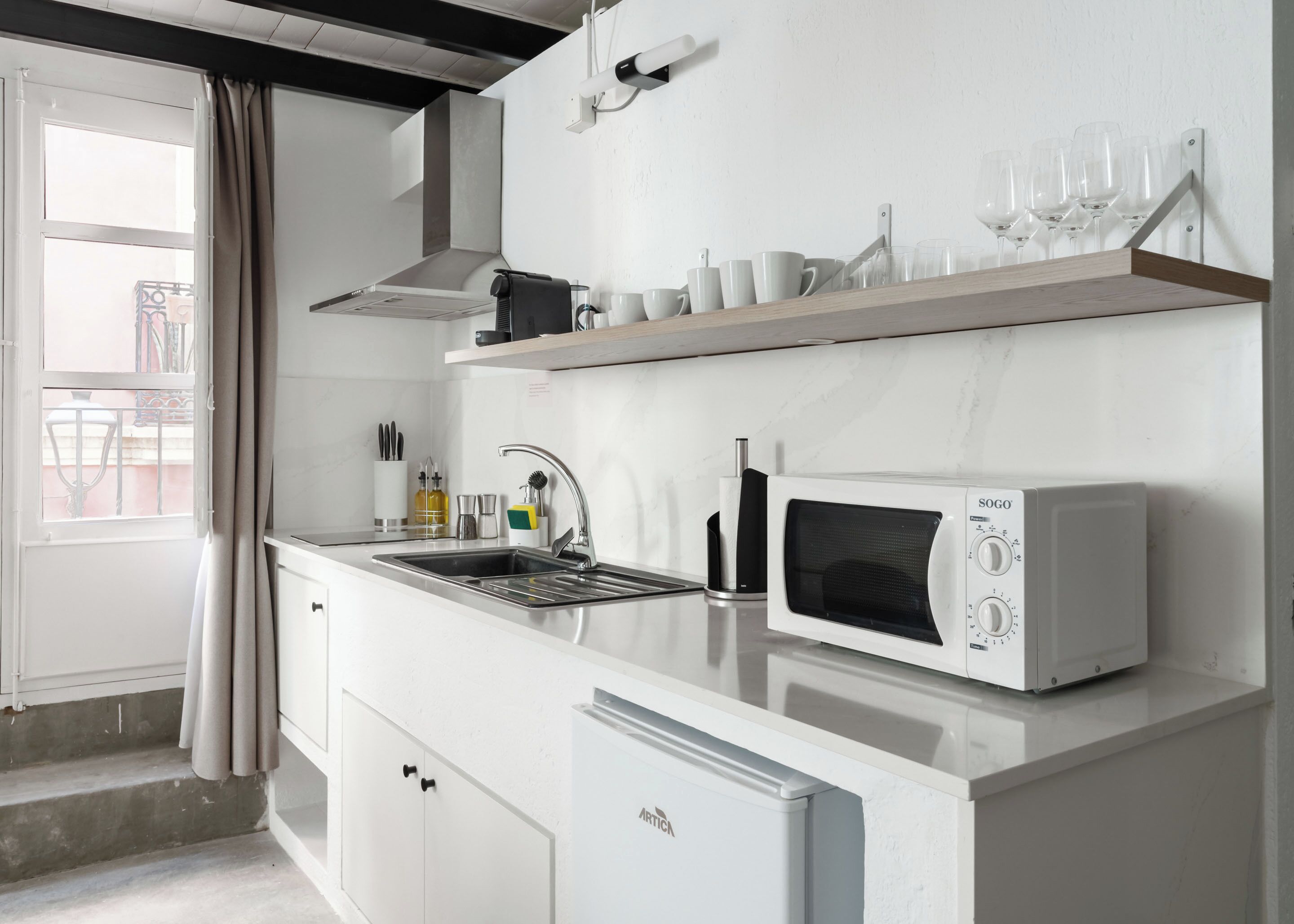 A modern kitchen with a built-in microwave, stainless steel sink, and a wooden shelf above the counter.