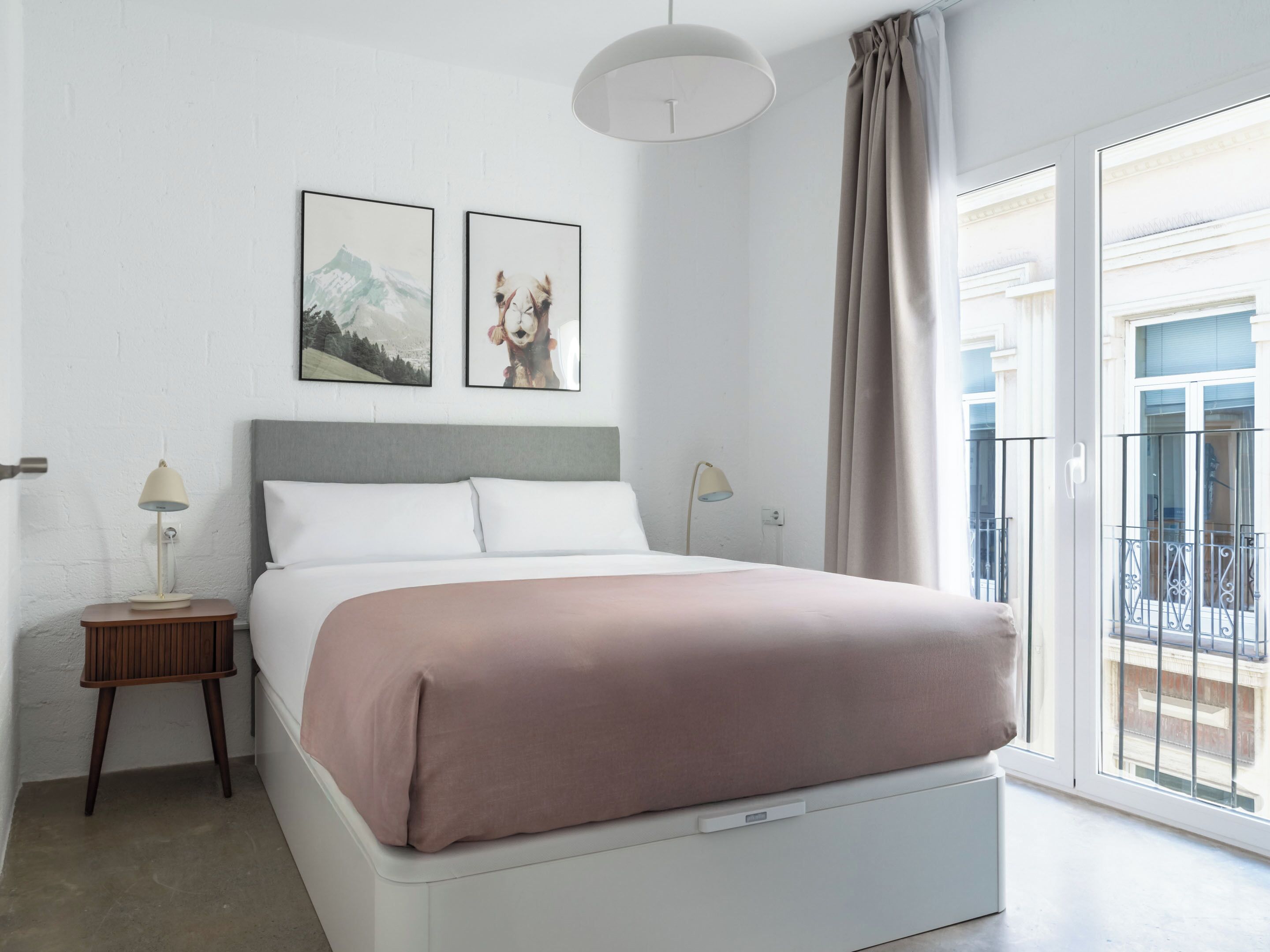 Un dormitorio con cama, dos mesitas de noche, lámpara de techo y ventana con vistas.