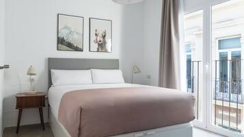 Un dormitorio con cama, dos mesitas de noche, lámpara de techo y ventana con vistas.