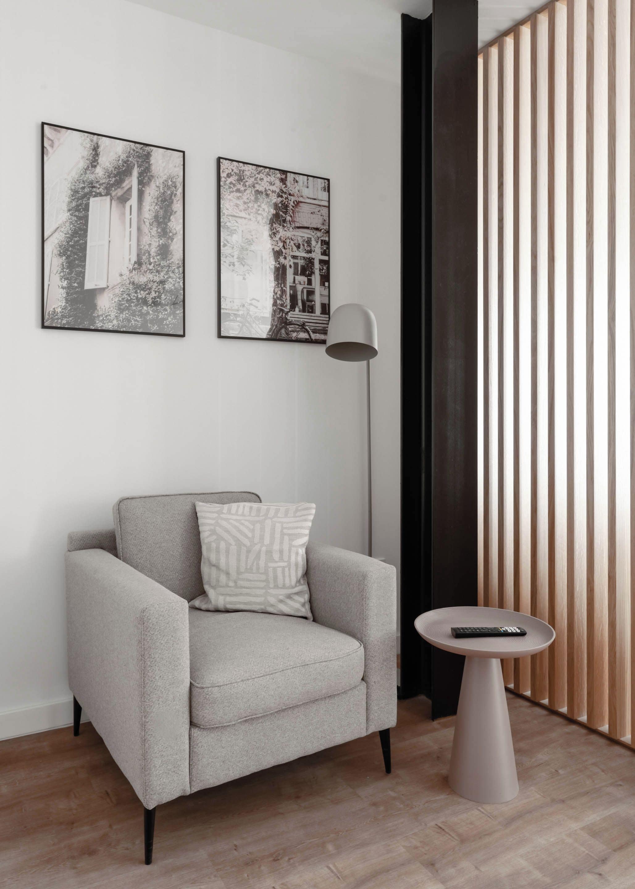 A modern living room with a grey armchair, a round side table, and two framed pictures on the wall.