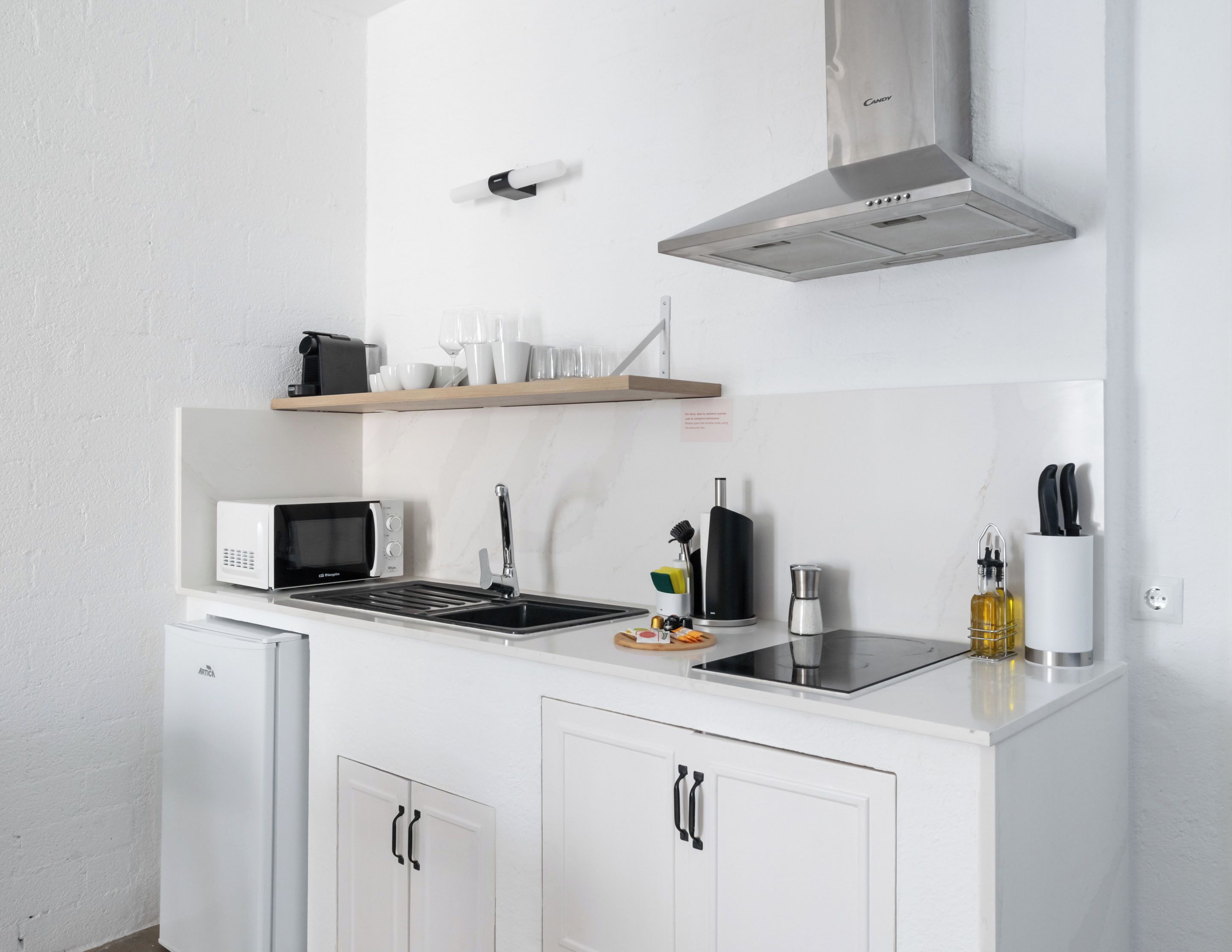 A compact kitchenette with a microwave, sink, and stainless steel range hood.