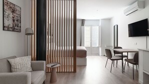 A modern living room with a sofa, a coffee table, a TV, and a dining area with chairs and a table. - Limehome Almeria C. Hernán Cortés (Almeria)