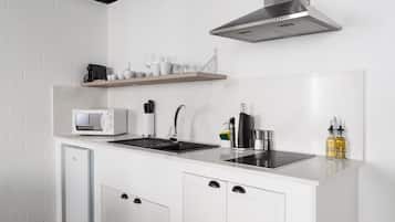 Una cocina compacta con microondas integrado, un fregadero y una campana extractora de acero inoxidable. Hay un refrigerador pequeño y un estante con tazas y vasos.
