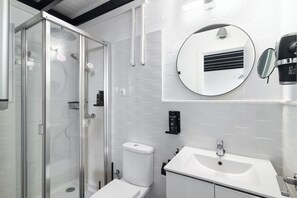 Un baño moderno con ducha envuelta en cristal, inodoro, lavamanos y espejo redondo.