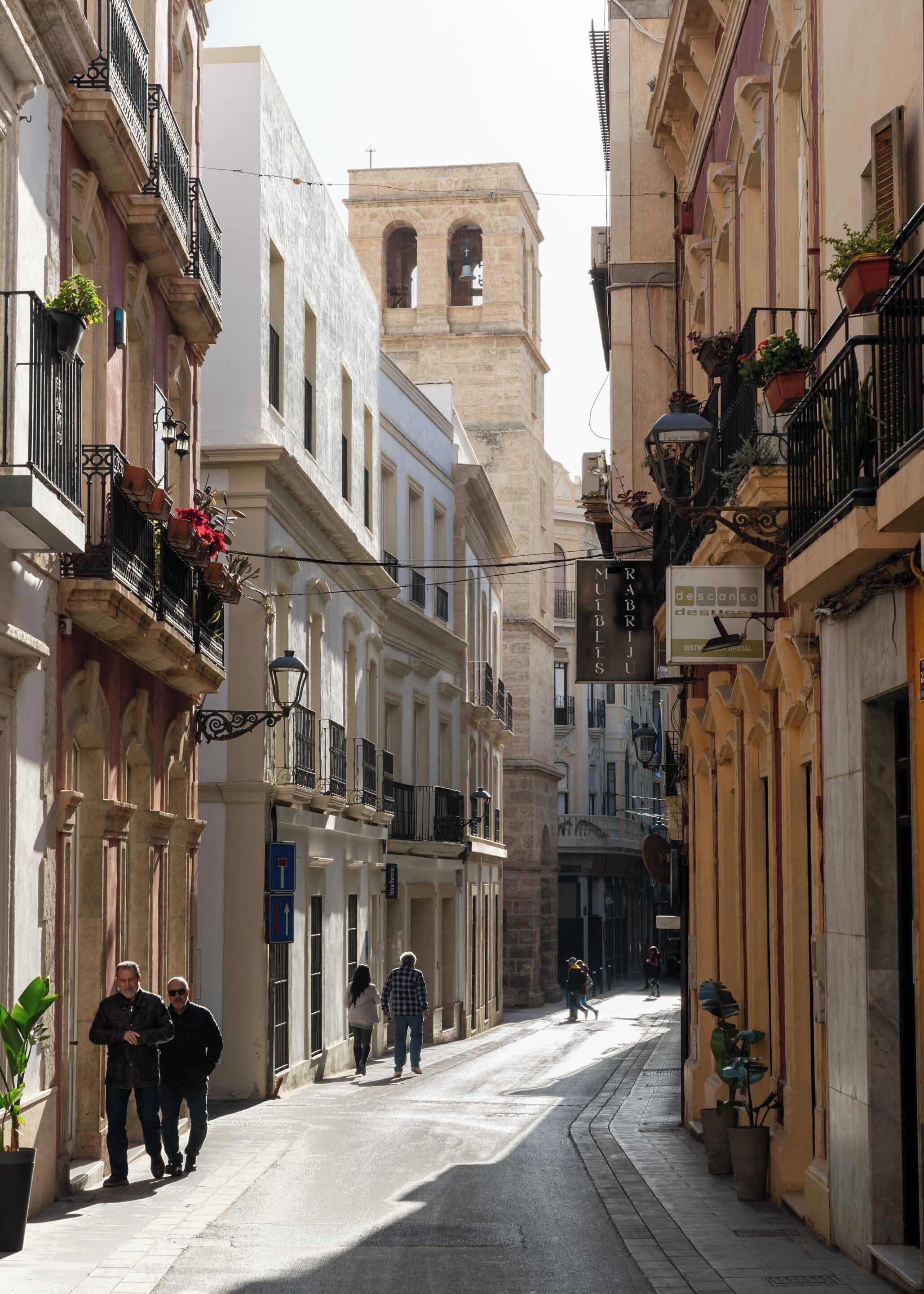 Un carrer estret flanquejat per edificis històrics, alguns amb balcons i plantes en testos.