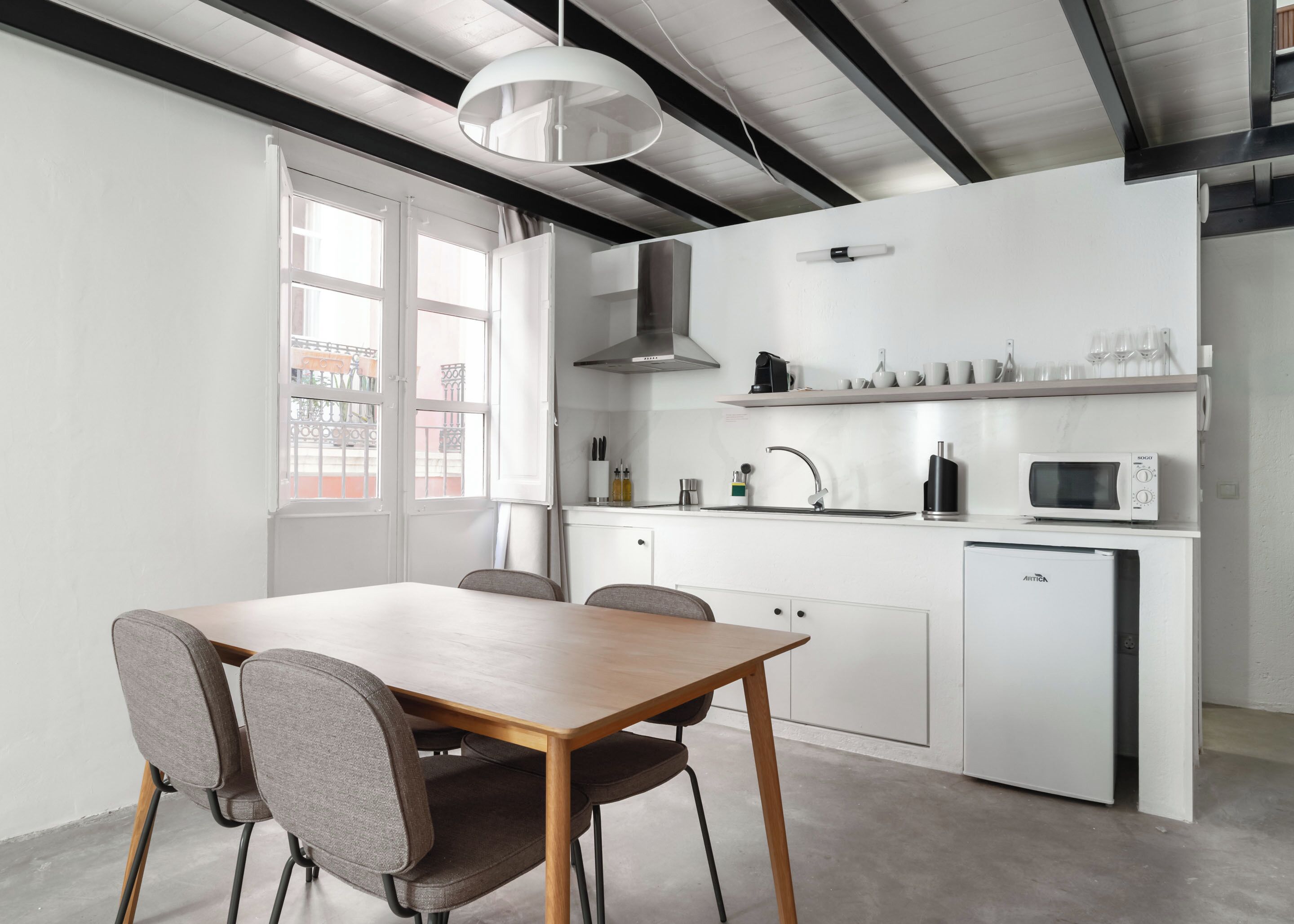 Una cocina moderna con armarios blancos, microondas integrado y un refrigerador compacto.