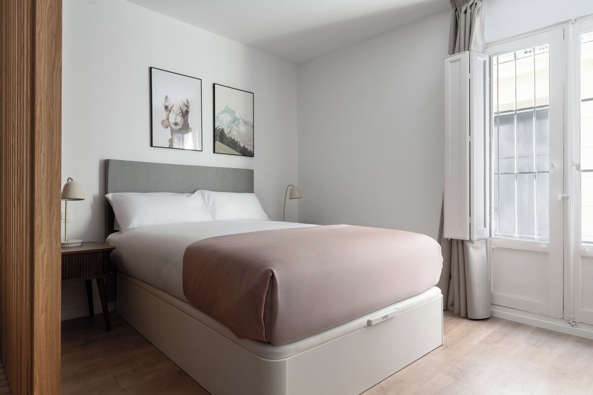 A modern bedroom with a bed, a nightstand, a lamp, and two framed pictures on the wall.