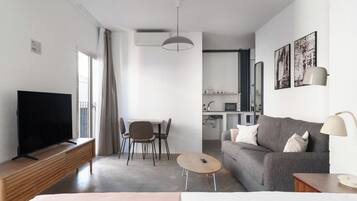 Un salon moderne doté d’un téléviseur à écran plat, d’un canapé gris, d’une petite table basse ronde et d’un coin repas avec une table et des chaises.