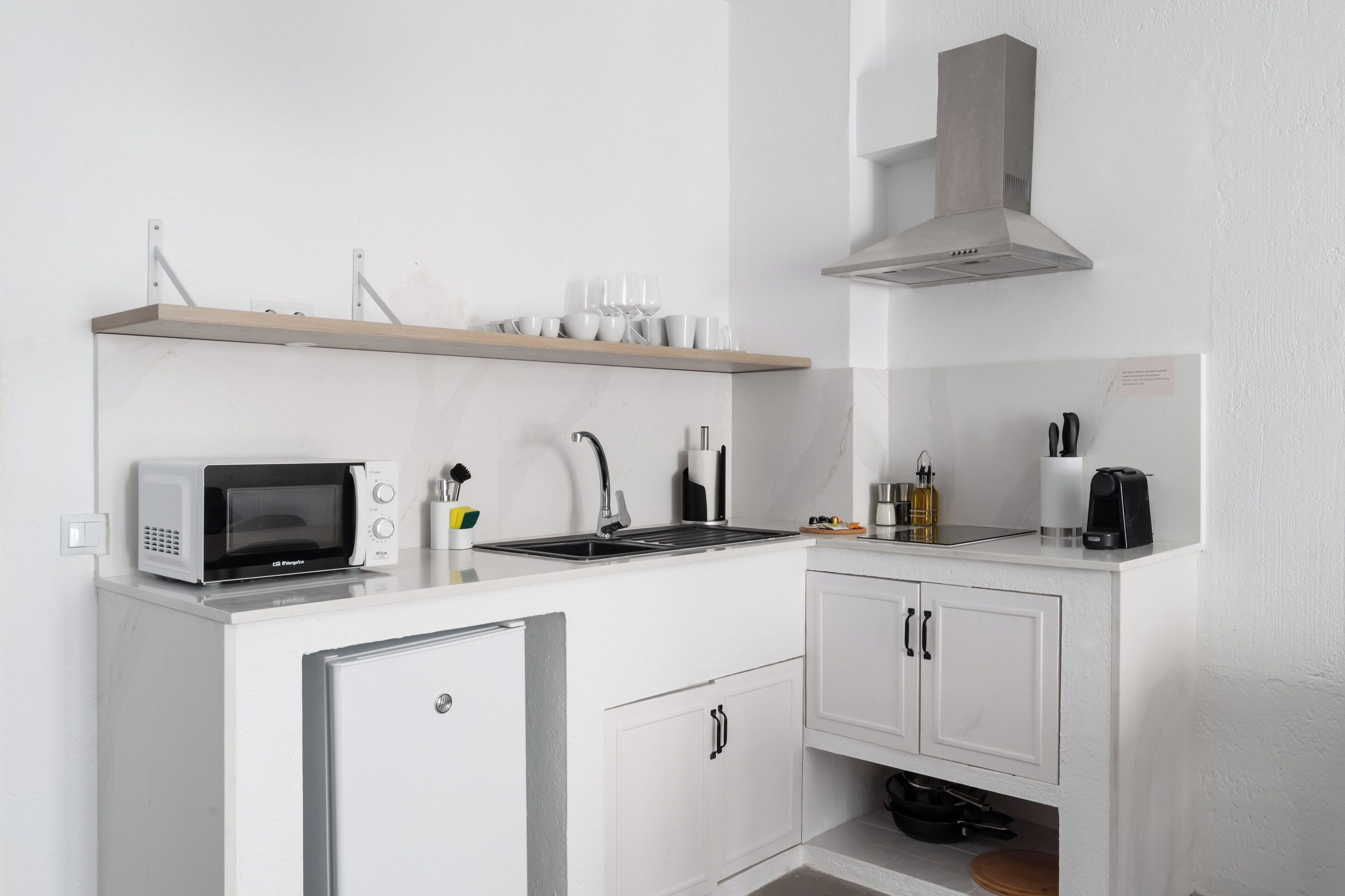 A compact kitchen with a microwave, sink, and a built-in stove. There is a shelf above the microwave and a cabinet below the sink.