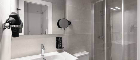 A modern bathroom with a white sink, a mirror, a hairdryer, and a glass-enclosed shower.