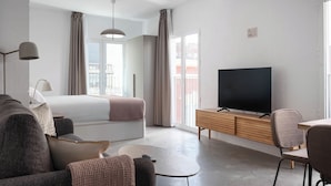 A modern hotel room with a bed, a TV, a sofa, a coffee table, and a dining area. - Limehome Almeria C. Hernán Cortés (Almeria)