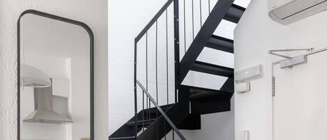 Eine moderne Küche mit weißen Schränken, einer schwarzen Treppe und einem Spiegel.