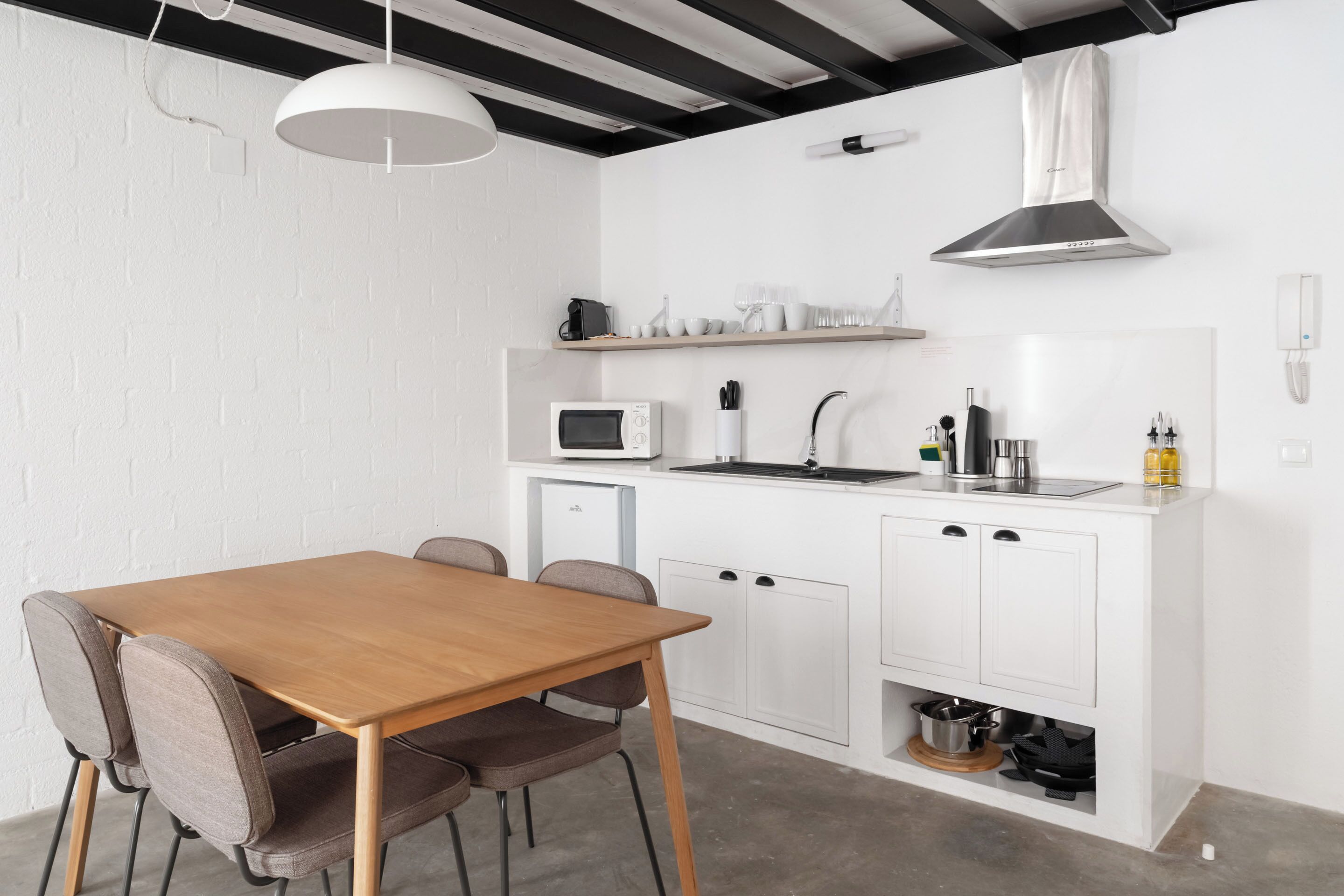 Cocina compacta con mesa y sillas de madera, muebles blancos, microondas y horno empotrado.
