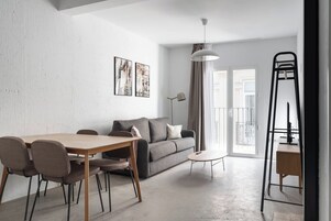 Una sala de estar moderna con una mesa de comedor de madera, un sofá gris y una escalera metálica negra.
