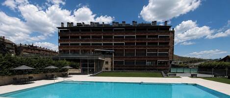 A modern building with a pool, outdoor seating, and a clear sky.