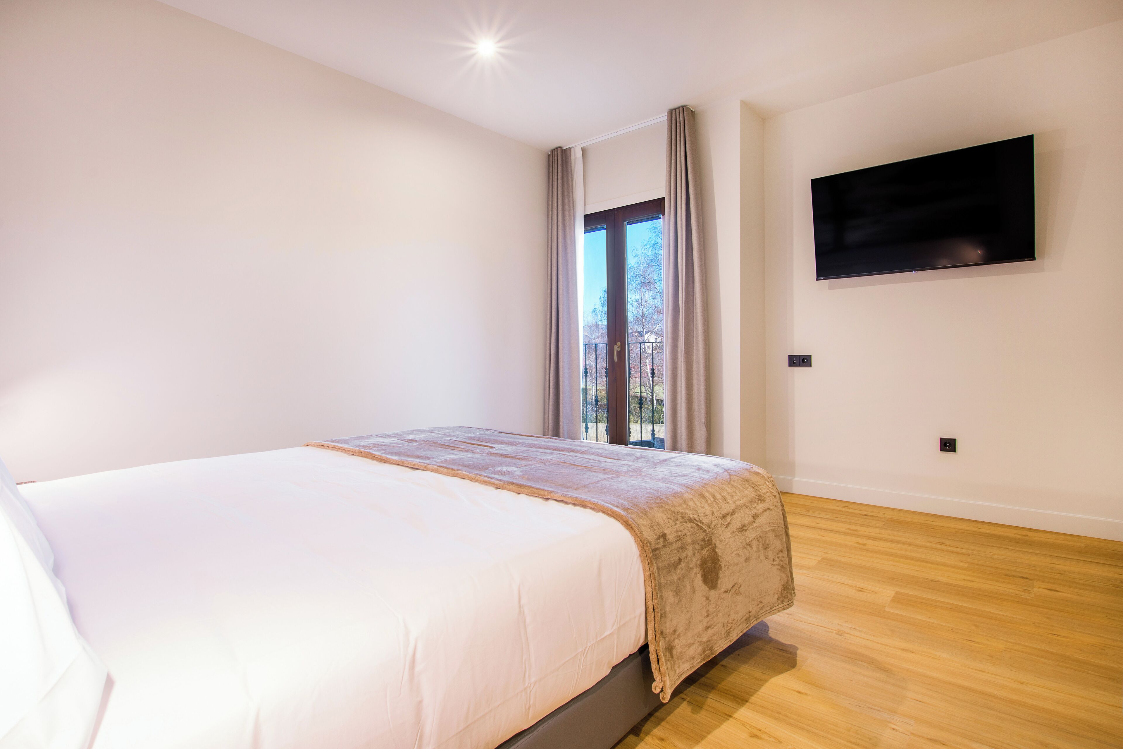 A bedroom with a bed, a TV mounted on the wall, and a window with curtains.