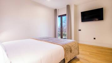 A bedroom with a bed, a TV mounted on the wall, and a window with curtains.