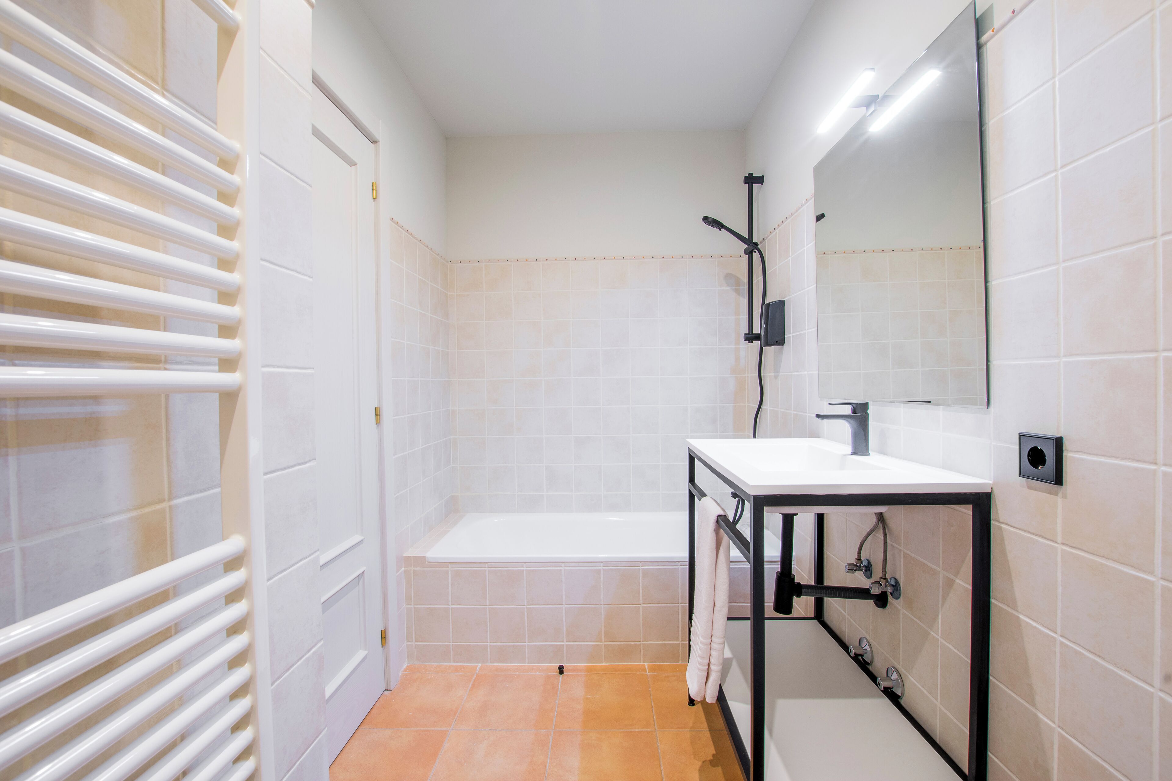 A modern bathroom with a white bathtub, a sink with a mirror, and a towel rack.