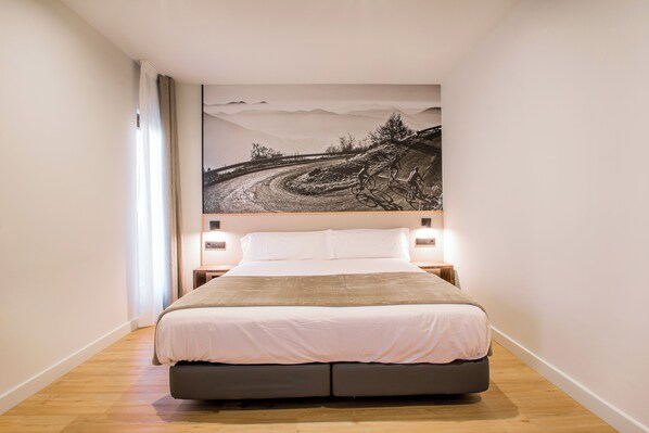 A bedroom with a large bed, a view of a winding road, and a mountain landscape. - Hotel Llivia (Llívia)