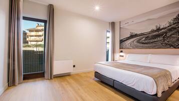 A bedroom with a large bed, a view of a building through a window, and a painting on the wall.