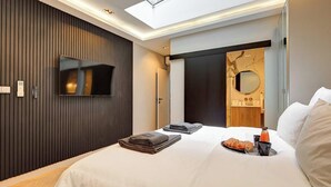 Camera d'albergo moderna con un letto grande, televisione a schermo piatto montata a parete, un lucernario e un bagno con specchio e lavandino.