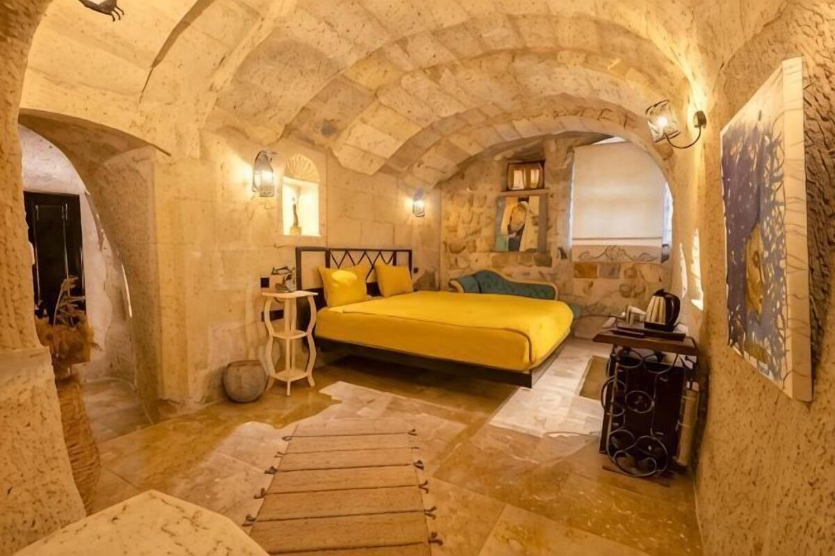 A room with a bed, a small table, a lamp, and a painting on the wall.