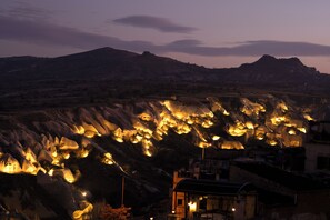 A mountainous landscape at dusk with illuminated rock formations and a building with a sloped roof. - Volca Inn Cappadocia  (Nevsehir)