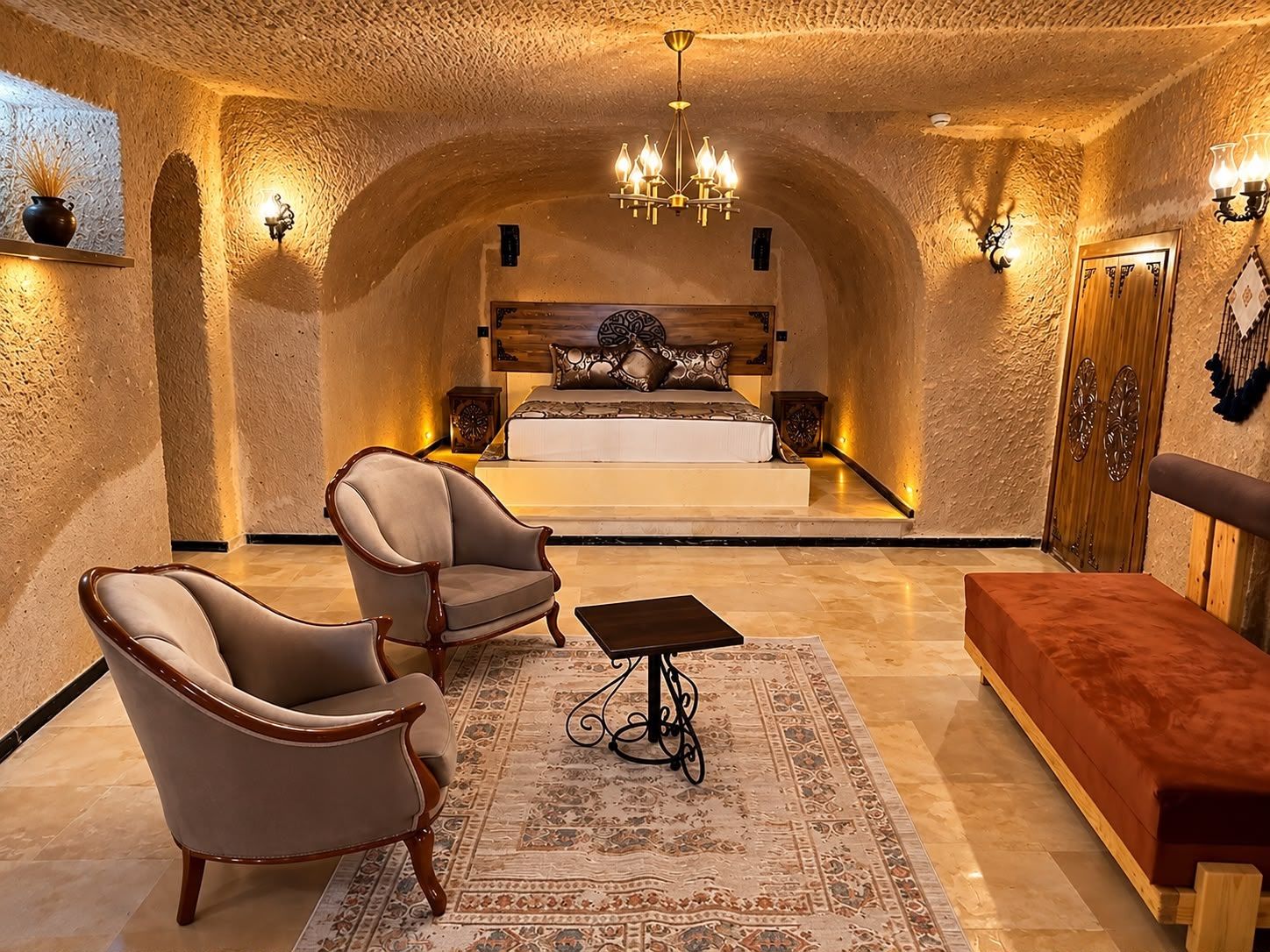 Un dormitorio lujoso con una cama grande, un área de descanso con un sofá y sillones, un armario de madera y una alfombra estampada.