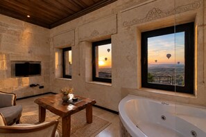 Une pièce avec une grande baignoire, une table en bois et un téléviseur fixé au mur.