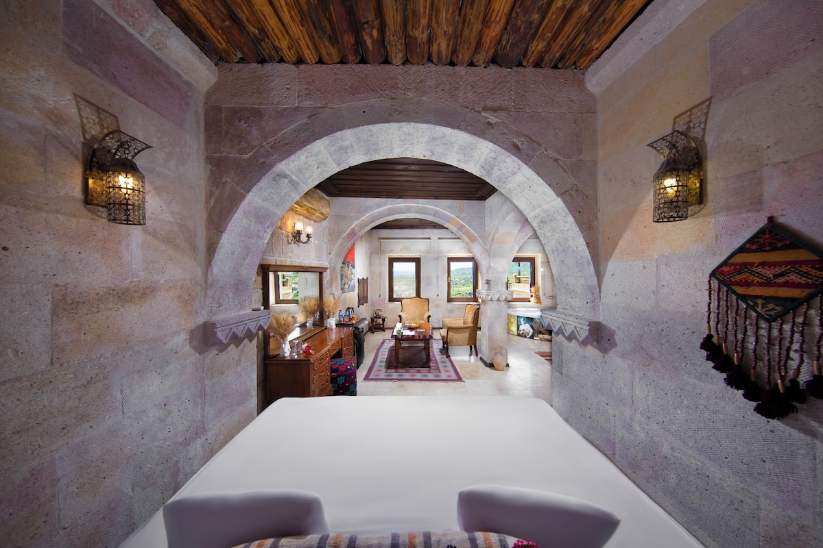 A room with a white table, two chairs, stone walls, wooden ceiling beams, and arched doorways.