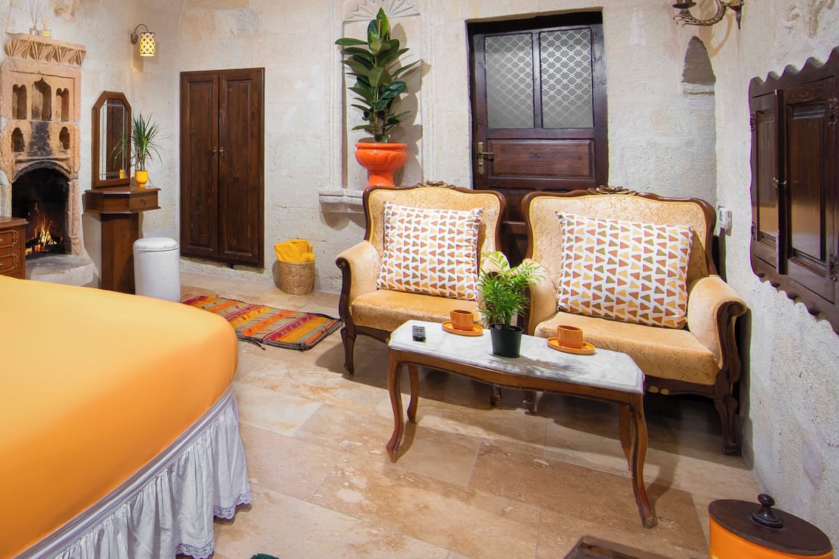 A traditional room with a bed, two sofas with patterned cushions, a small table with a plant, a fireplace, and a large wooden door.