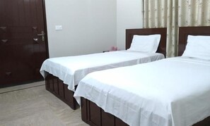 Two single beds with white bedspreads are positioned against a wall with a headboard.