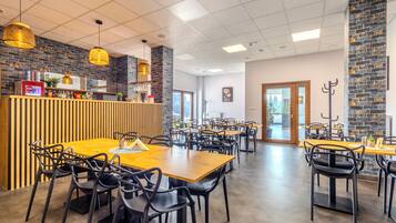 Un restaurante moderno con mesas de madera y sillas negras, una barra con refrigerador de Coca-Cola y una pared de ladrillo.