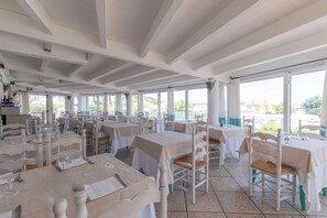 Un restaurante espacioso con varias mesas y sillas, ventanas amplias y vistas al exterior.