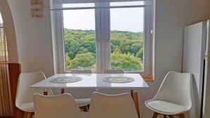 A dining area with a table and four chairs, a window with a view of a forest, and a hanging decoration with the words "Love" and "Laugh". - Charming 2-bedroom, family friendly cottage in Miskolc at the Bükk Mountains (Miskolc)
