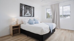 A modern bedroom with a large bed, a bedside table, a nightstand, and a view of the outdoors through a window. - Hidden Gem - 150m from Urunga Sea Lido (Urunga)