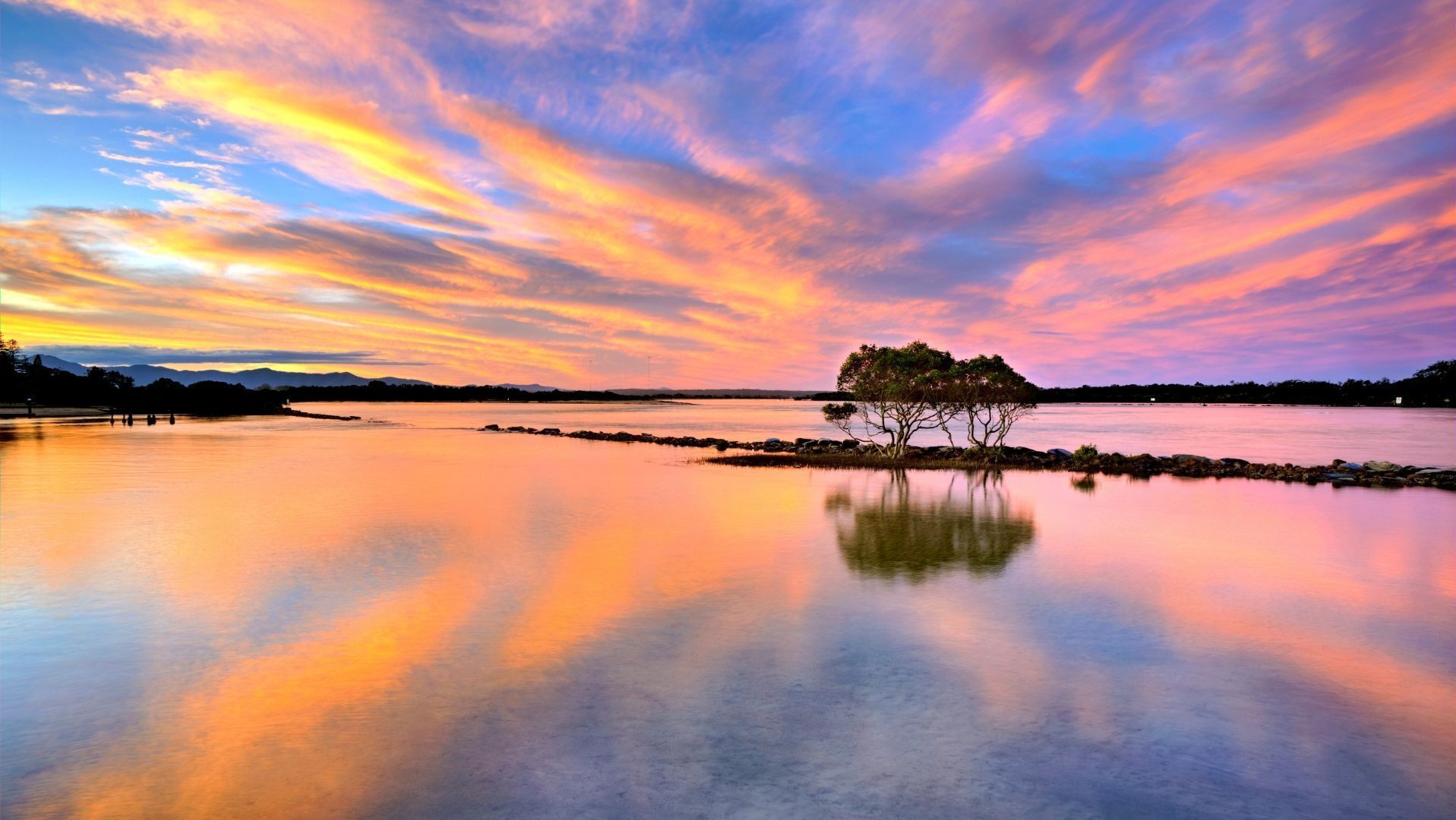 A tranquil lakeside scene with a single tree reflecting in calm waters, surrounded by a colorful sky.