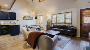 A spacious living area with a high ceiling, a dining table, a sofa, and a kitchen area with dark cabinets.
