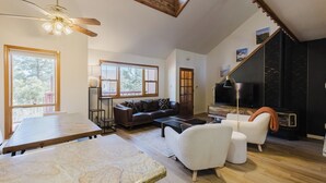 A spacious living area with a wooden ceiling, a large window, a sofa, a coffee table, and a fireplace.