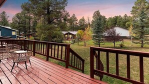 A wooden deck with outdoor furniture, overlooking a grassy area with trees and a building in the background.