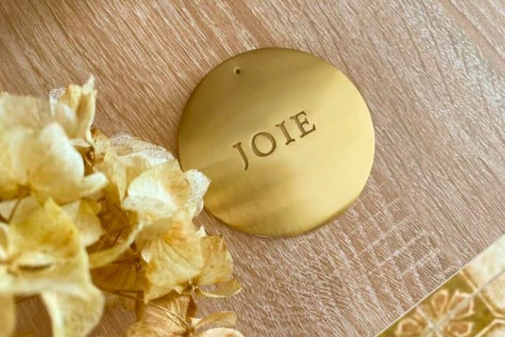 A gold nameplate with the name "JOIE" on a wooden surface.
