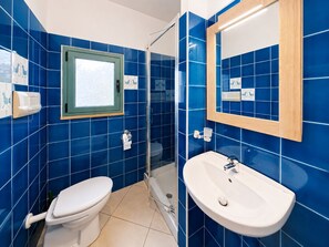 A bathroom with blue tiles, a white toilet, a glass shower enclosure, and a white sink with a mirror.