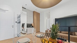 Een moderne keuken met witte kasten, een eetgedeelte met een houten tafel, en een zithoek met een bank en een televisie.