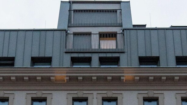 Een meerhoog gebouw in klassieke stijl, met een centrale ingang met decoratieve boog en een balkon.