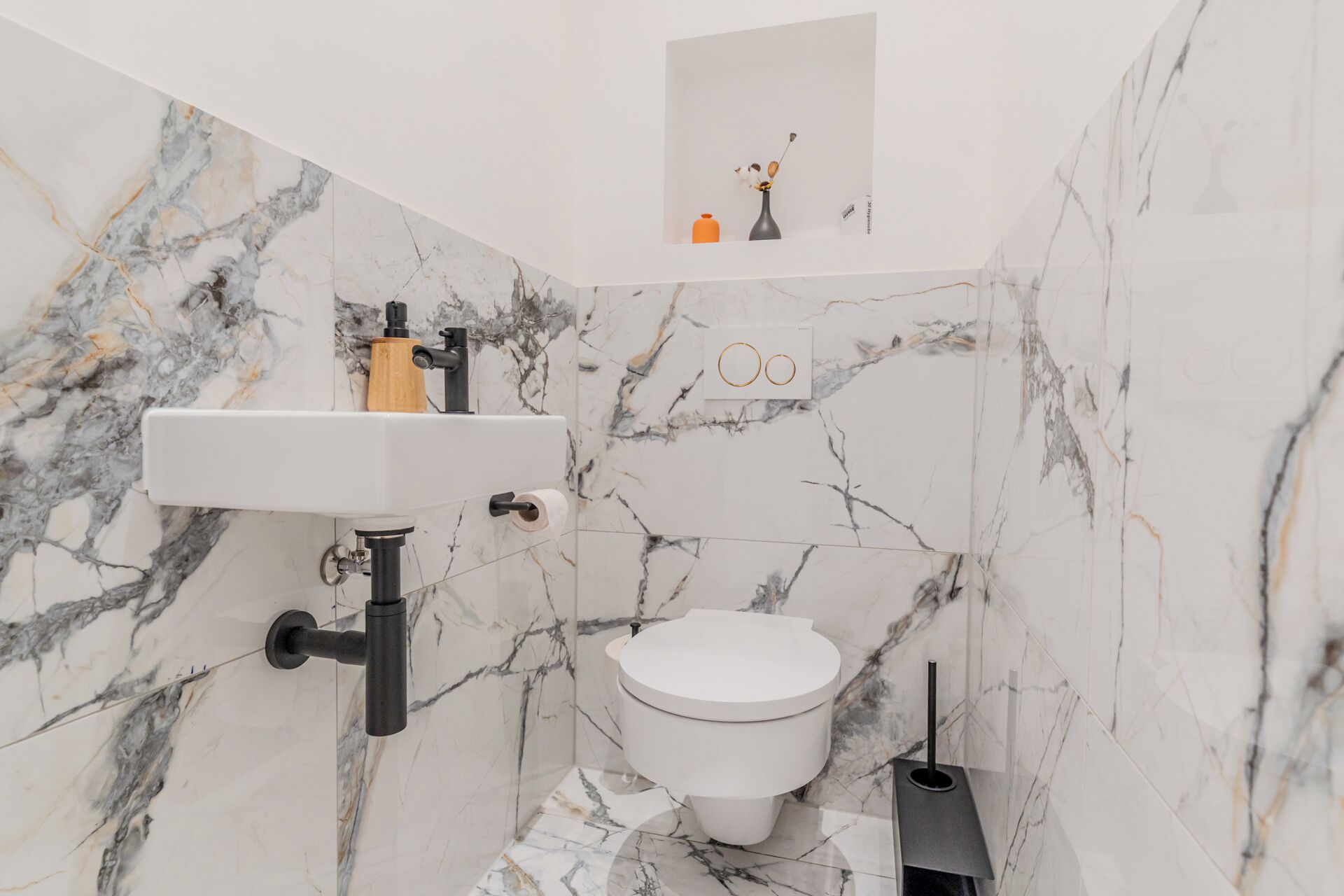 A bathroom with a marble wall, white sink, and toilet.